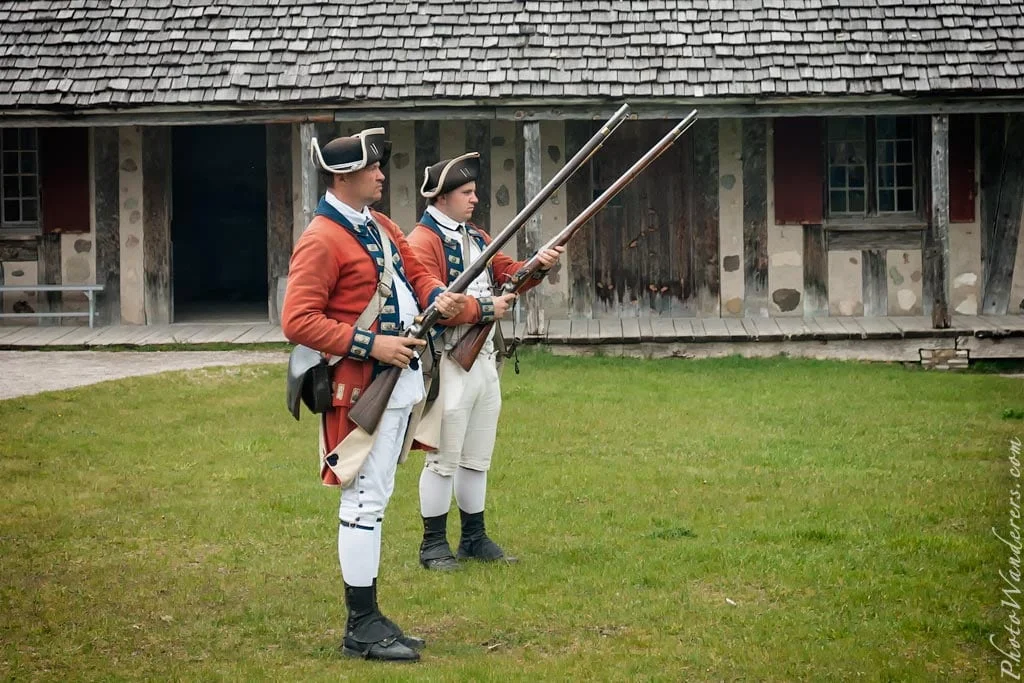 Reenactors in British redcoat uniforms, standing inside the fort