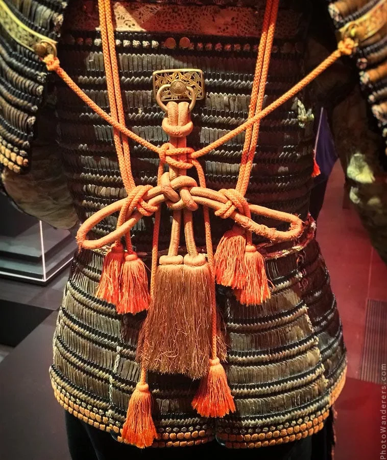 The cords up close — orange silk, knotted and tasseled at the back, over rows of dark lacquered plates.