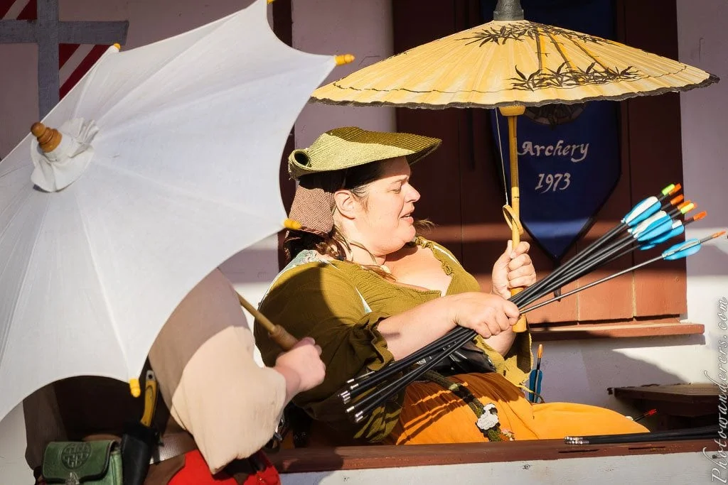 The archery keeper — arrows in one hand, parasol in the other, deeply comfortable with the chaos around her.