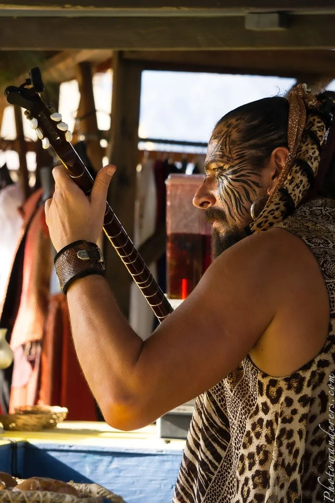 A street musician with tiger-stripe face paint and a lute.